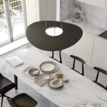 Flat dark disc pendant with a round glowing centre above a marble island