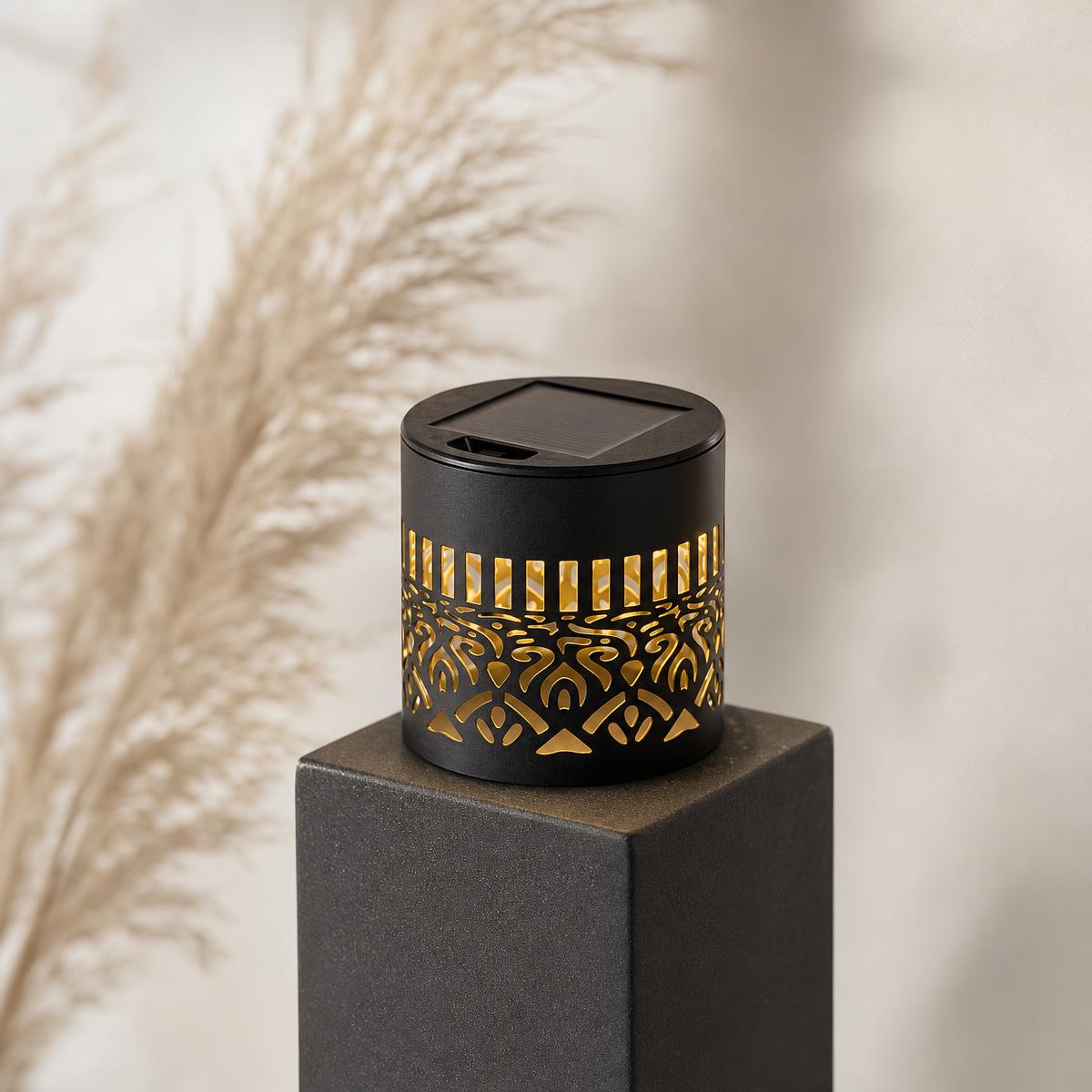 Black solar wall light with cut out mandala pattern atop an outdoor pedestal