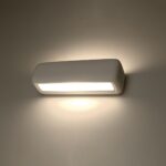 White rounded rectangle wall light glowing warmly with a bright diffuser strip on a beige wall