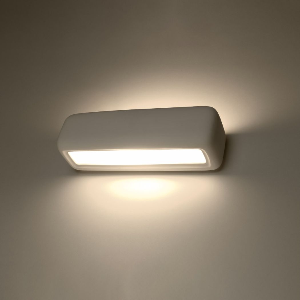 White rounded rectangle wall light glowing warmly with a bright diffuser strip on a beige wall