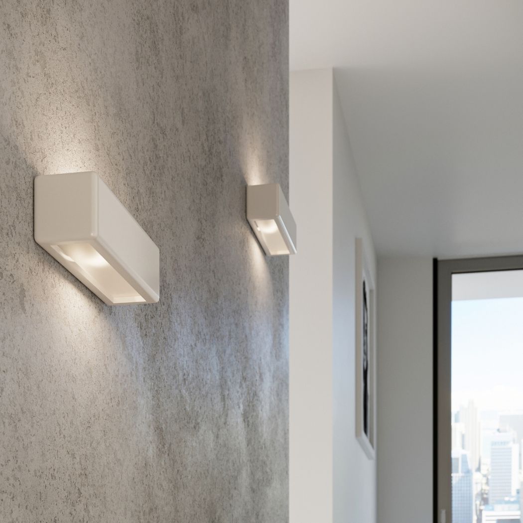 Two white rectangular wall lights on a textured grey wall near a window with a city view