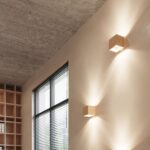 Two cube shaped wooden wall lights on a wall with a concrete ceiling and bookshelf