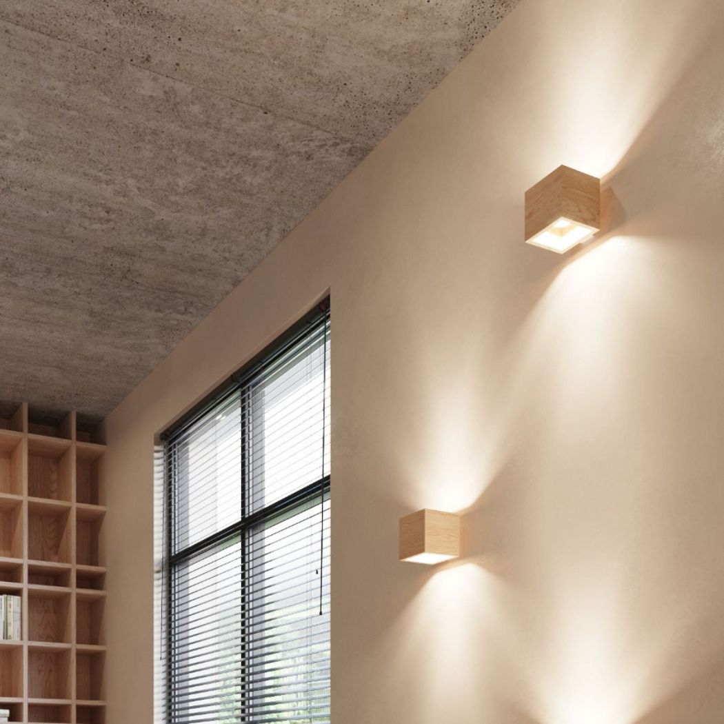 Two cube shaped wooden wall lights on a wall with a concrete ceiling and bookshelf