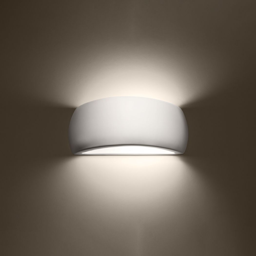 Glossy white half moon wall light glowing with light spreading up and down a dark wall