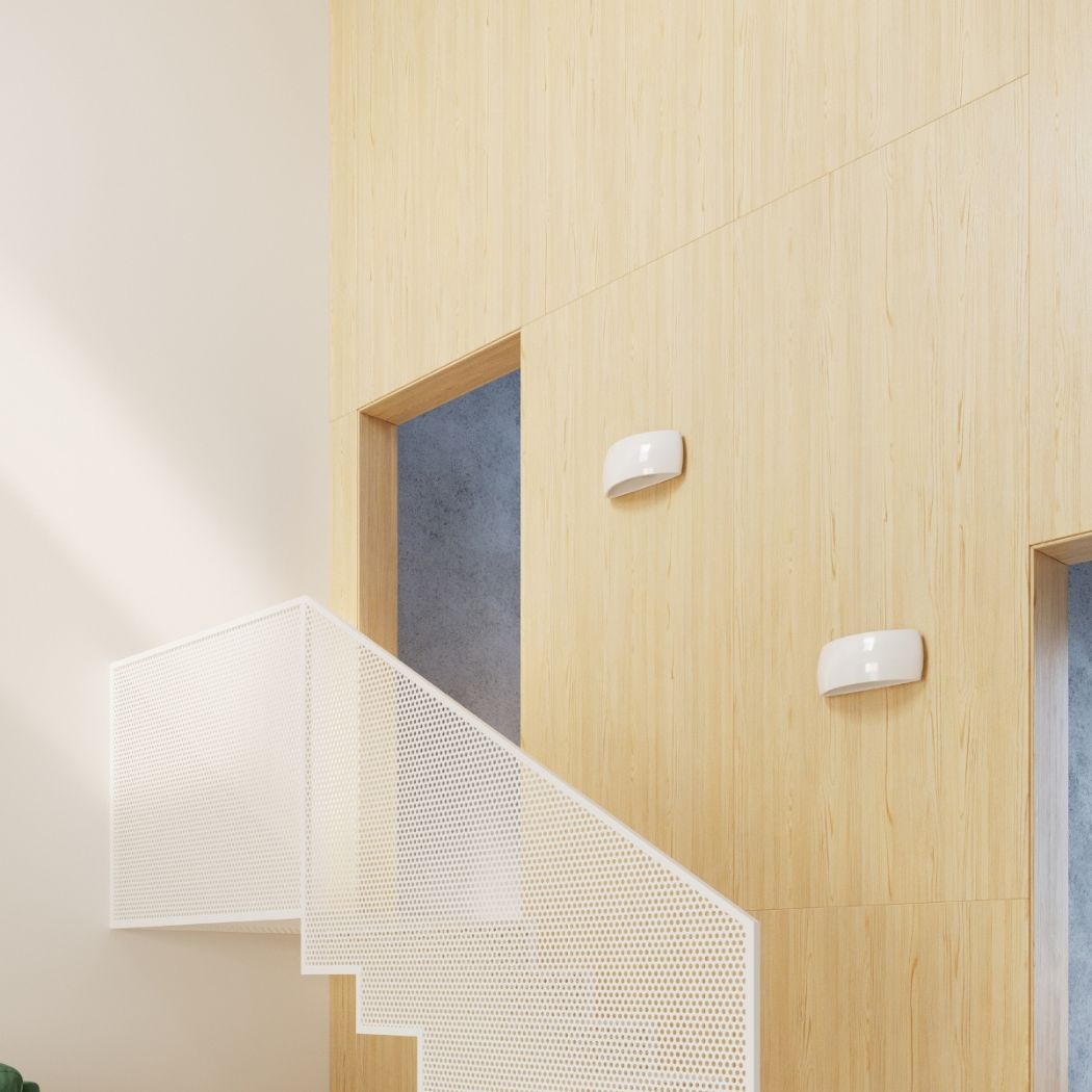 Two white half moon wall lights on a wood panelled wall beside a perforated staircase