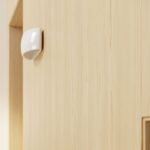 Small glossy white half moon wall light mounted on a light wood panelled surface