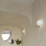 Curved plaster hallway with round mirrors and two white globe wall lights