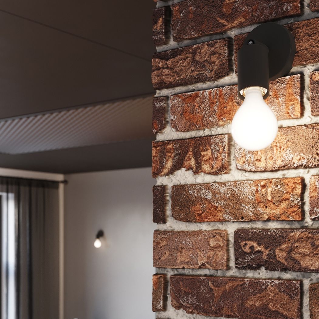 Black wall spotlight with a glowing bulb mounted on a brick wall