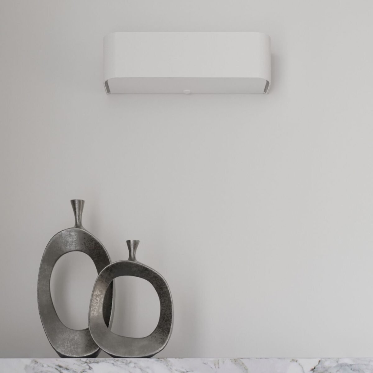 White wall light above a marble console with silver abstract sculptures