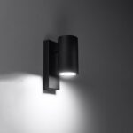 Black rectangular wall bracket with a cylindrical shade lit against a dark wall