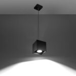 Black cube pendant light hanging on a thin cable glowing on a grey wall