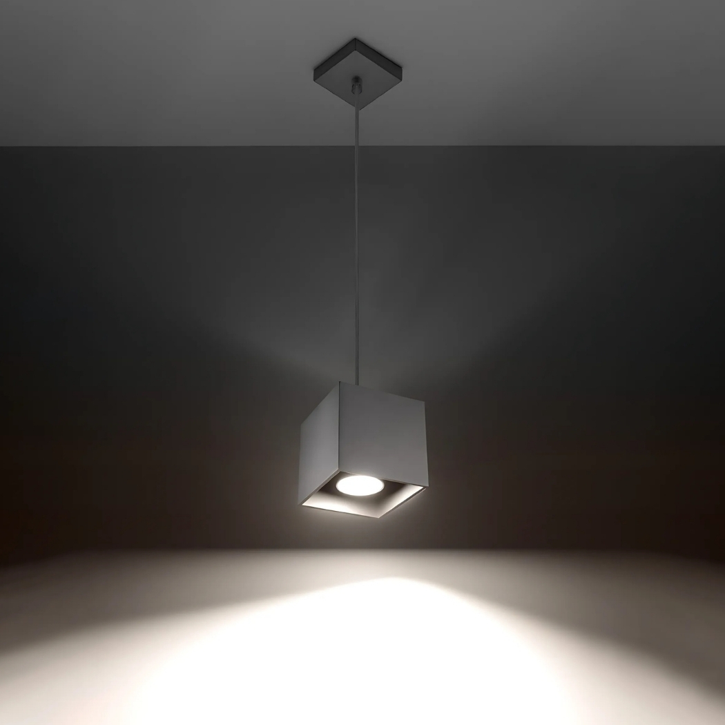 Grey cube pendant light hanging on a thin cable glowing on a dark ceiling