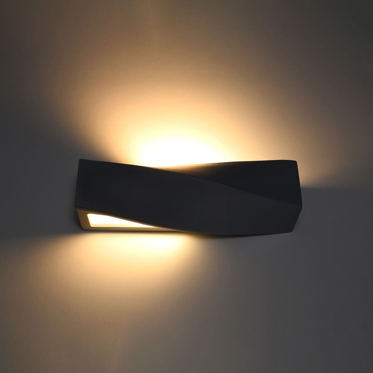 Twisted black wall light casting warm light upward and downward