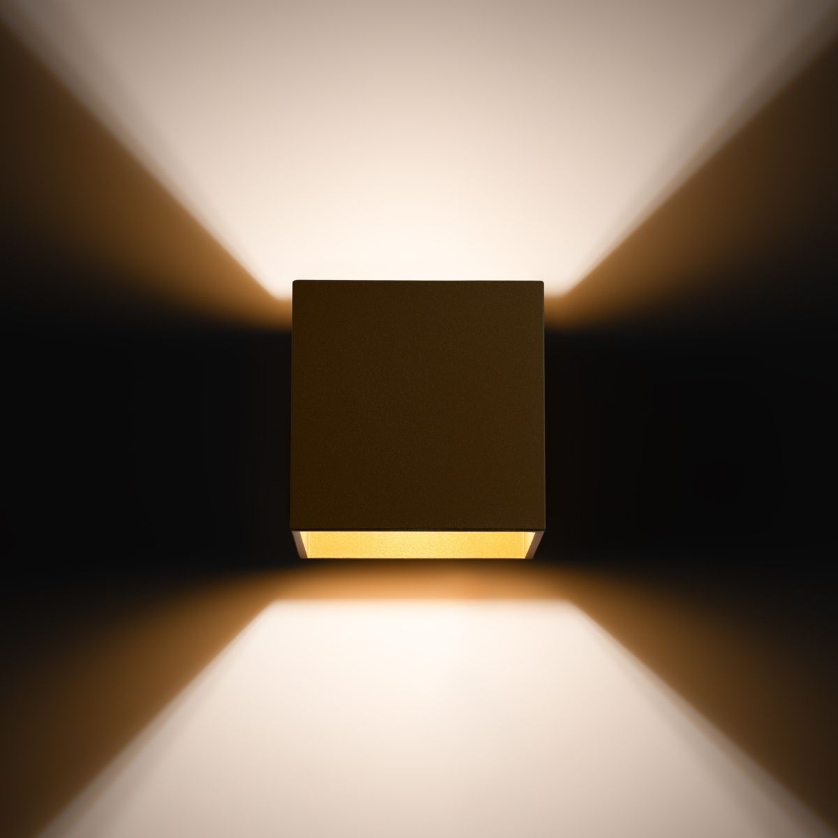 Gold cube wall light glowing with warm light spreading up and down a dark wall