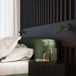 Green ribbed spotlight wall light above a dark green ottoman and bedside table