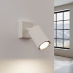 White ribbed adjustable spotlight wall light casting a warm downward beam