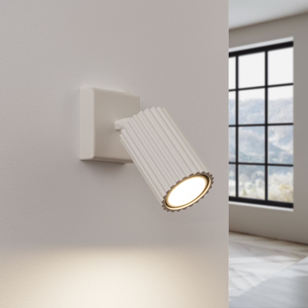 White ribbed adjustable spotlight wall light casting a warm downward beam