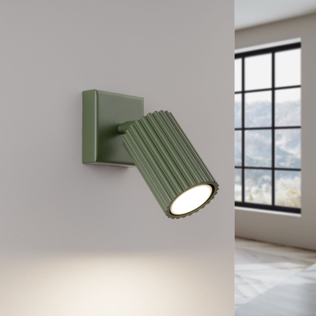 Green ribbed adjustable spotlight wall light casting a warm downward beam