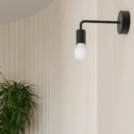 Black steel wall light with bare bulb above a potted plant near a wall