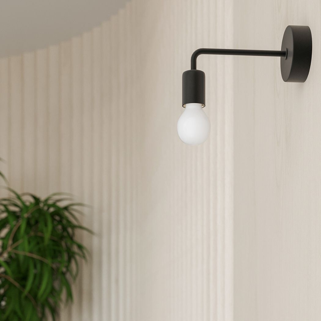 Black steel wall light with bare bulb above a potted plant near a wall