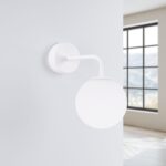 White glass globe wall light with a curved arm, switched off, near a window