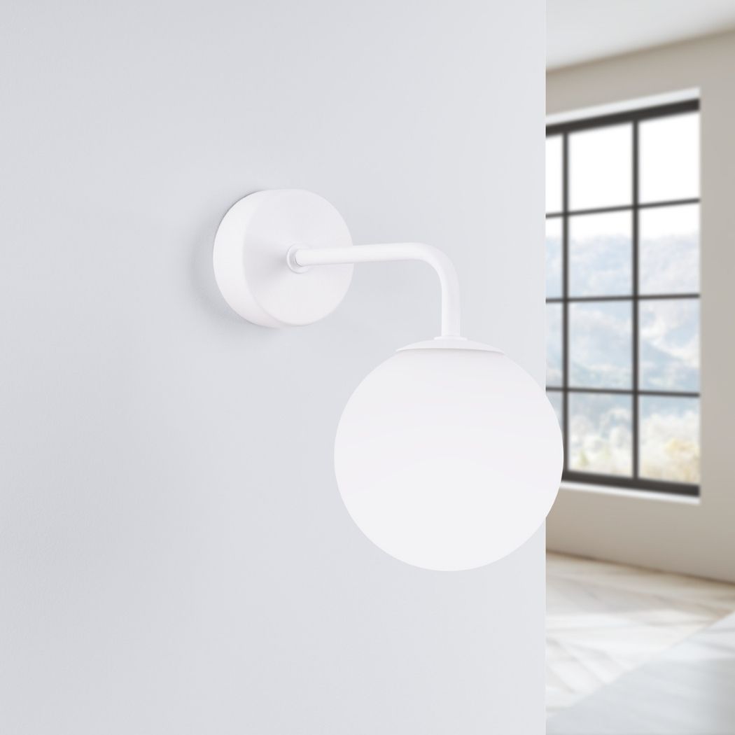 White glass globe wall light with a curved arm, switched off, near a window