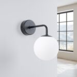 Black wall light with a round frosted glass globe beside a window