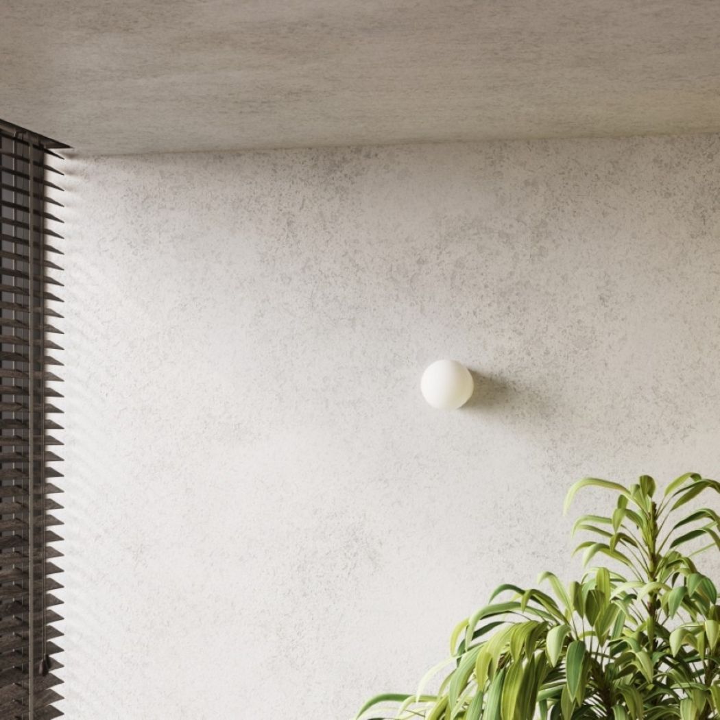 Small round glass ball wall light on a textured wall beside tall green leaves