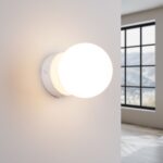 White round glass ball wall light glowing warm beside a large window