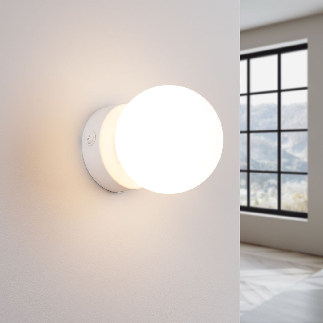 White round glass ball wall light glowing warm beside a large window