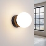 Bronze round glass ball wall light glowing warm beside a large window