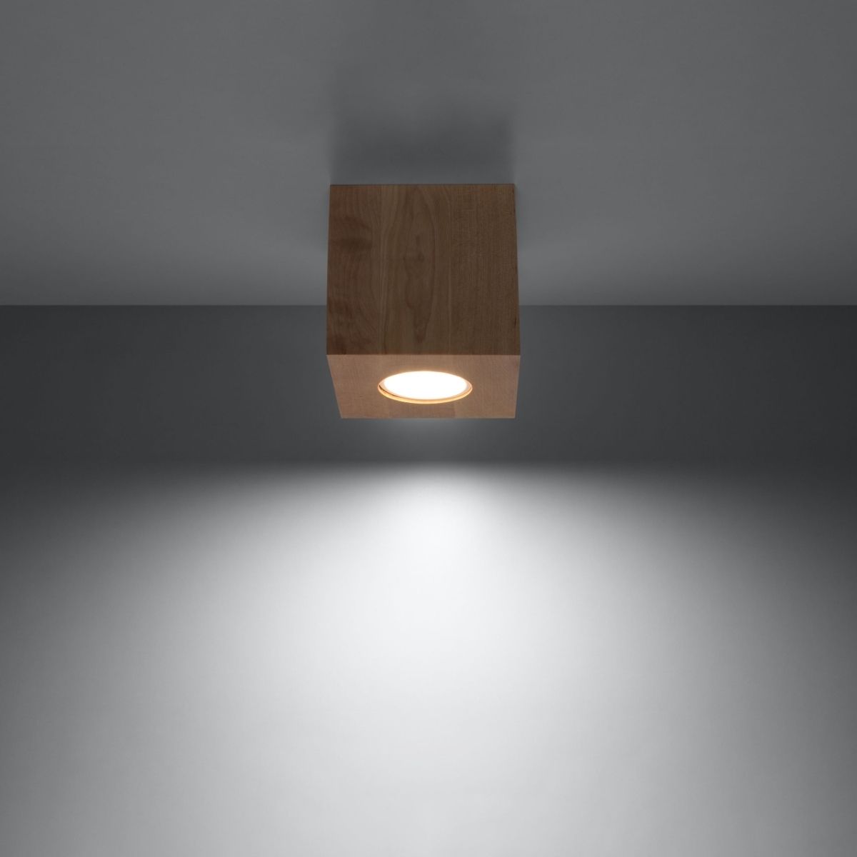 Wood cube ceiling spotlight casting a downward beam on a grey wall