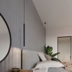 Slim black pendant hanging low beside a headboard with a round mirror and plant