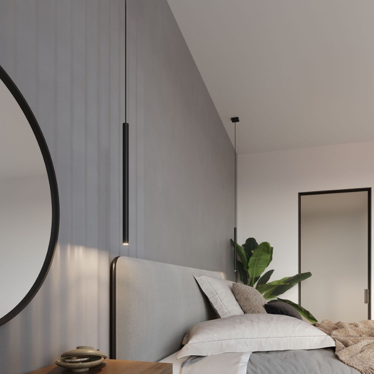 Slim black pendant hanging low beside a headboard with a round mirror and plant