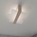 Close-up of the crossed wood beam and white glass panels of the ceiling light against the ceiling