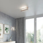 Angular wood and white ceiling light in the corner of a room with grey curtains and a window