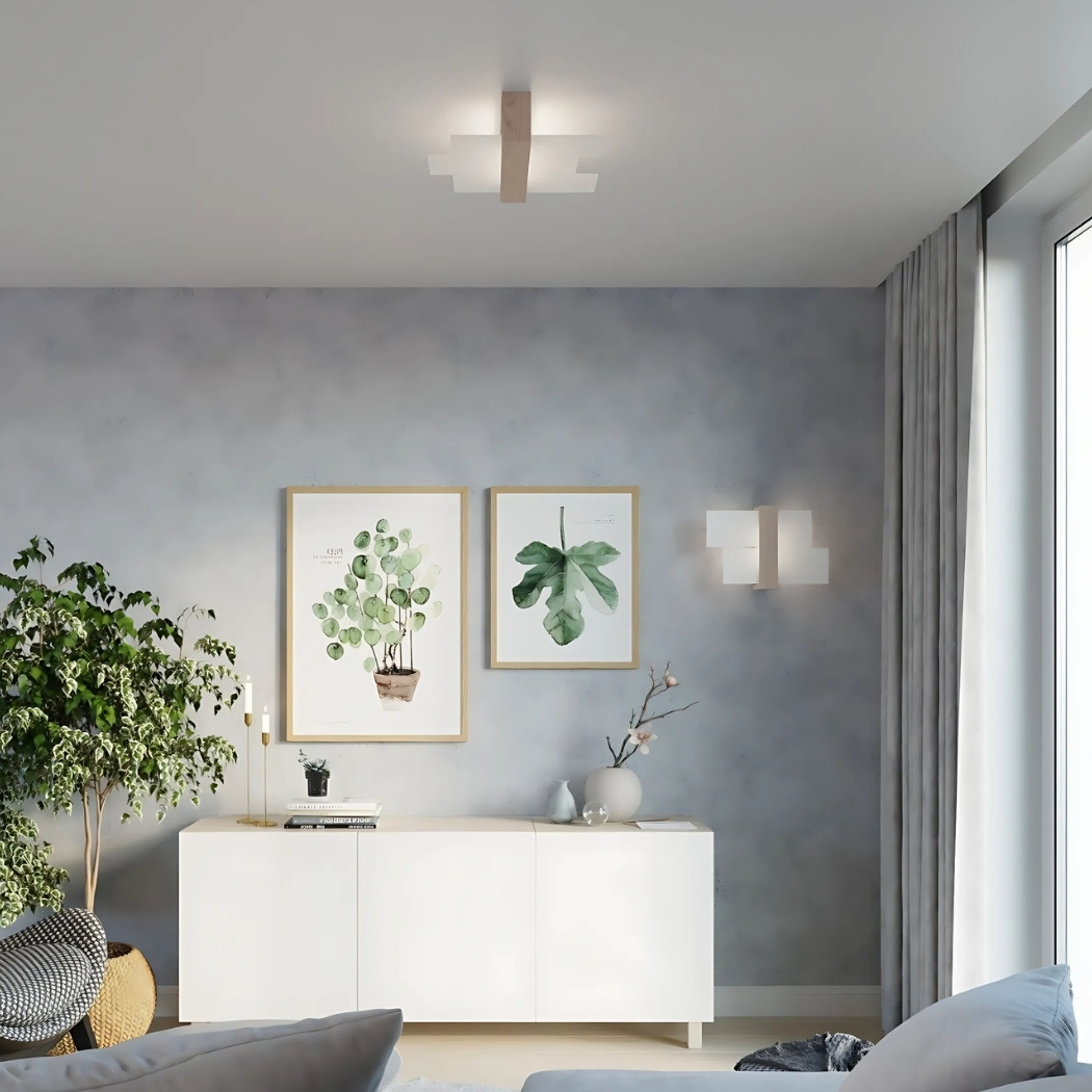 Cross shaped wood and white flush ceiling light above a white sideboard with framed botanical prints