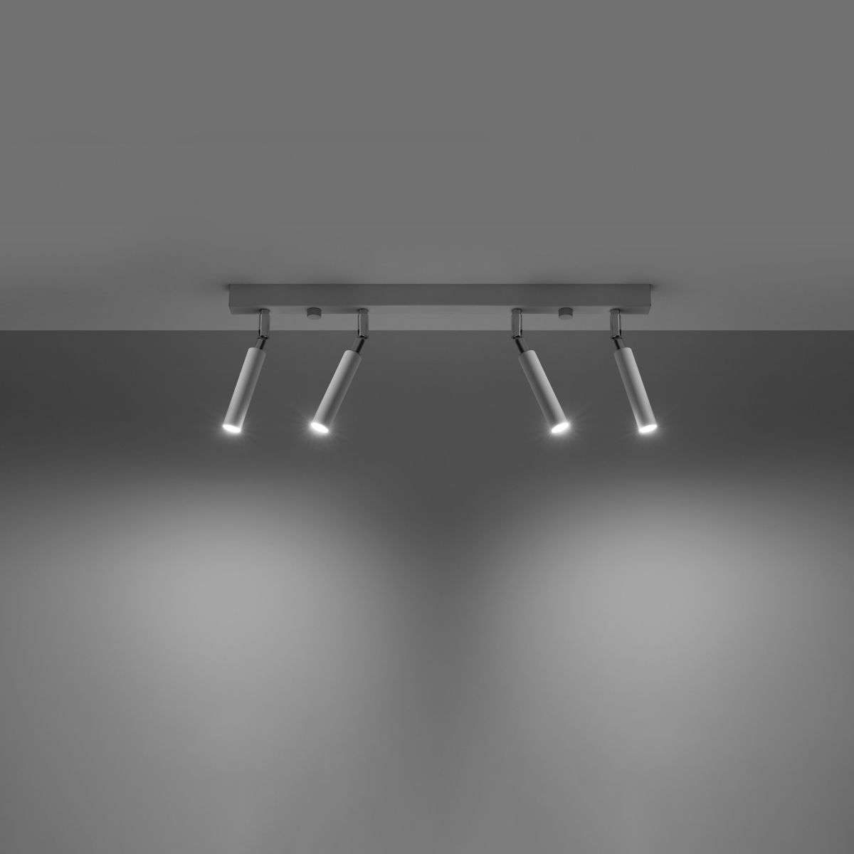 Black four spotlight ceiling bar lit against a plain gray backdrop