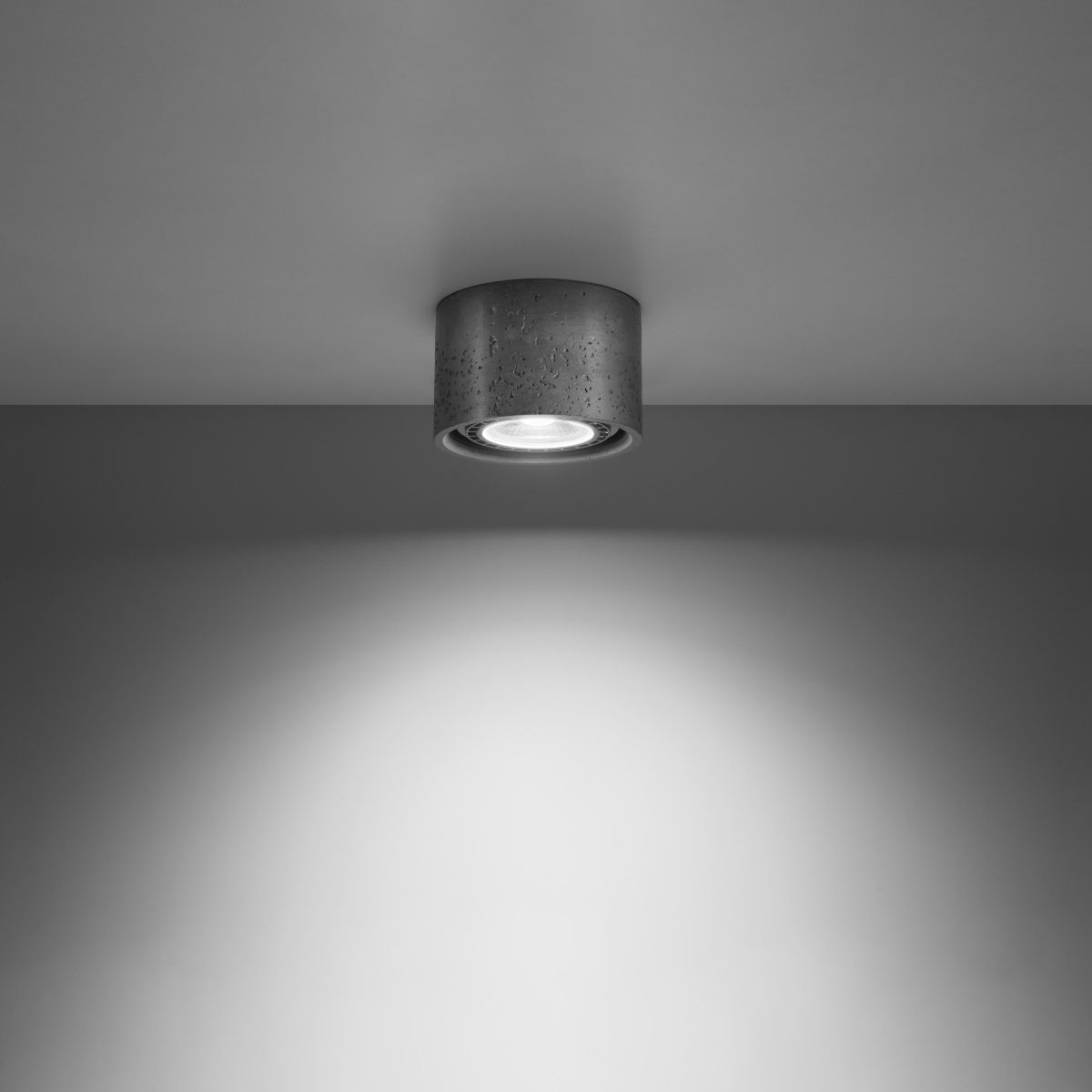 Single gray concrete cylinder ceiling spotlight glowing on a gray backdrop