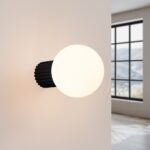 Black ribbed wall light base with a round frosted glass globe beside a window