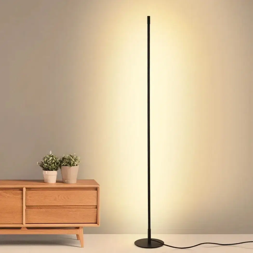 Tall black linear LED floor lamp glowing warm light against a wall