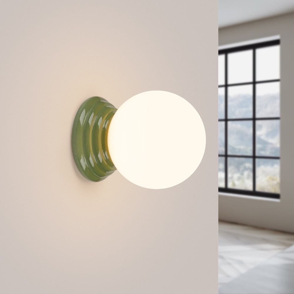 Green ribbed ceramic wall light with a round glass globe beside a window