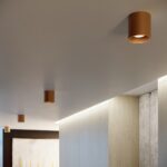 Cylindrical bronze spotlights lining a corridor ceiling above a stone wall panel