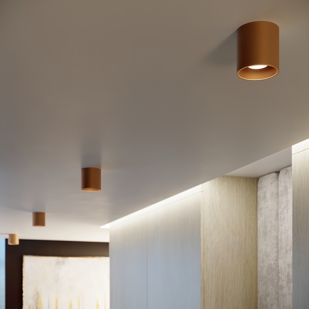 Cylindrical bronze spotlights lining a corridor ceiling above a stone wall panel