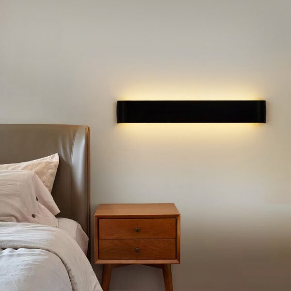 Black rectangular LED bar wall light glowing warmly above a nightstand
