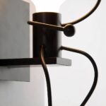 Close-up of a black wall light with curved arms holding a round diffuser