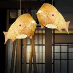 Two woven bamboo fish-shaped pendant lights hanging together against a bamboo backdrop