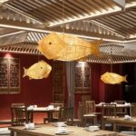 Woven bamboo fish-shaped pendant lights of varying sizes above a red-walled hall