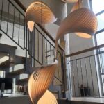 Curved wooden slat pendant lights spiraling above an indoor staircase