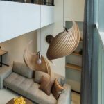 Two swirling wooden pendant lamps hanging above a grey sofa in a loft